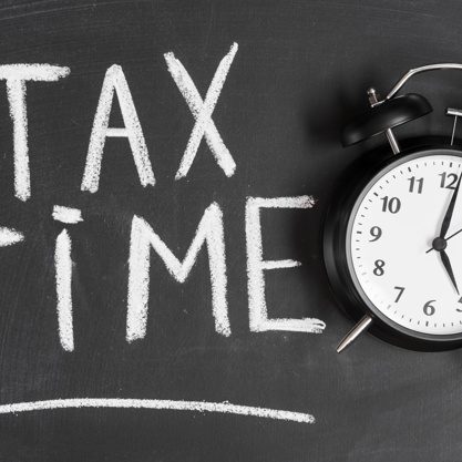 alarm-clock-near-tax-time-word-written-black-backboard-with-chalk_23-2147943569