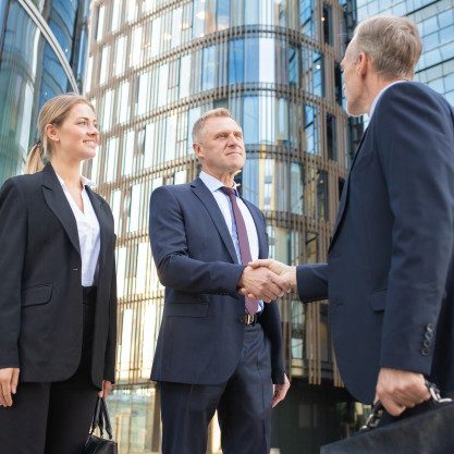 confident-business-partners-meeting-city-shaking-hands-near-office-building-low-angle-shot-cooperation-partnership-concept_74855-6893