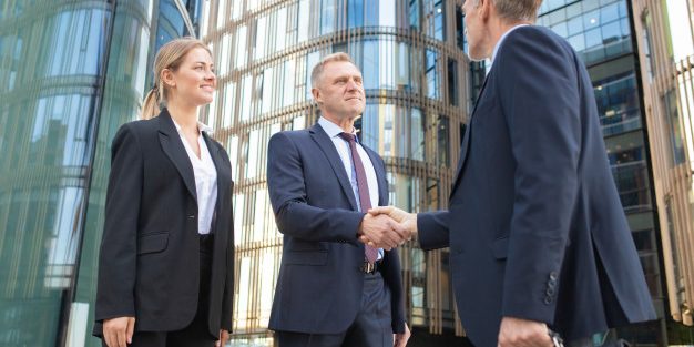 confident-business-partners-meeting-city-shaking-hands-near-office-building-low-angle-shot-cooperation-partnership-concept_74855-6893